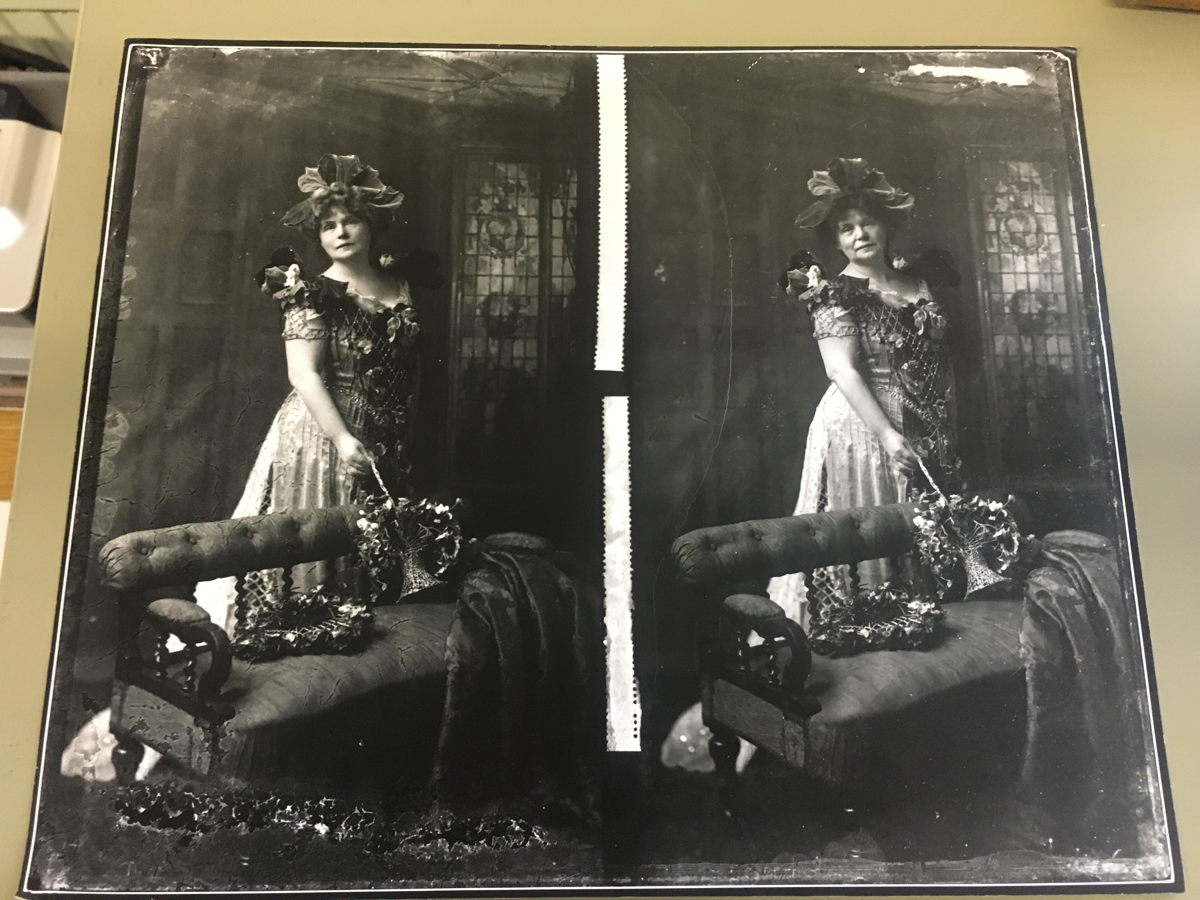Black and white photo of a woman in a formal dress and hat, standing by an ornate chair, holding a bouquet. The image appears as two near-identical side-by-side prints.