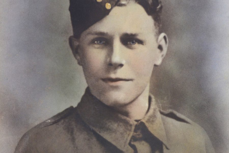 A young soldier in an old-fashioned military uniform and a side cap, looking directly at the camera. The image is colourised and has a soft, faded background.