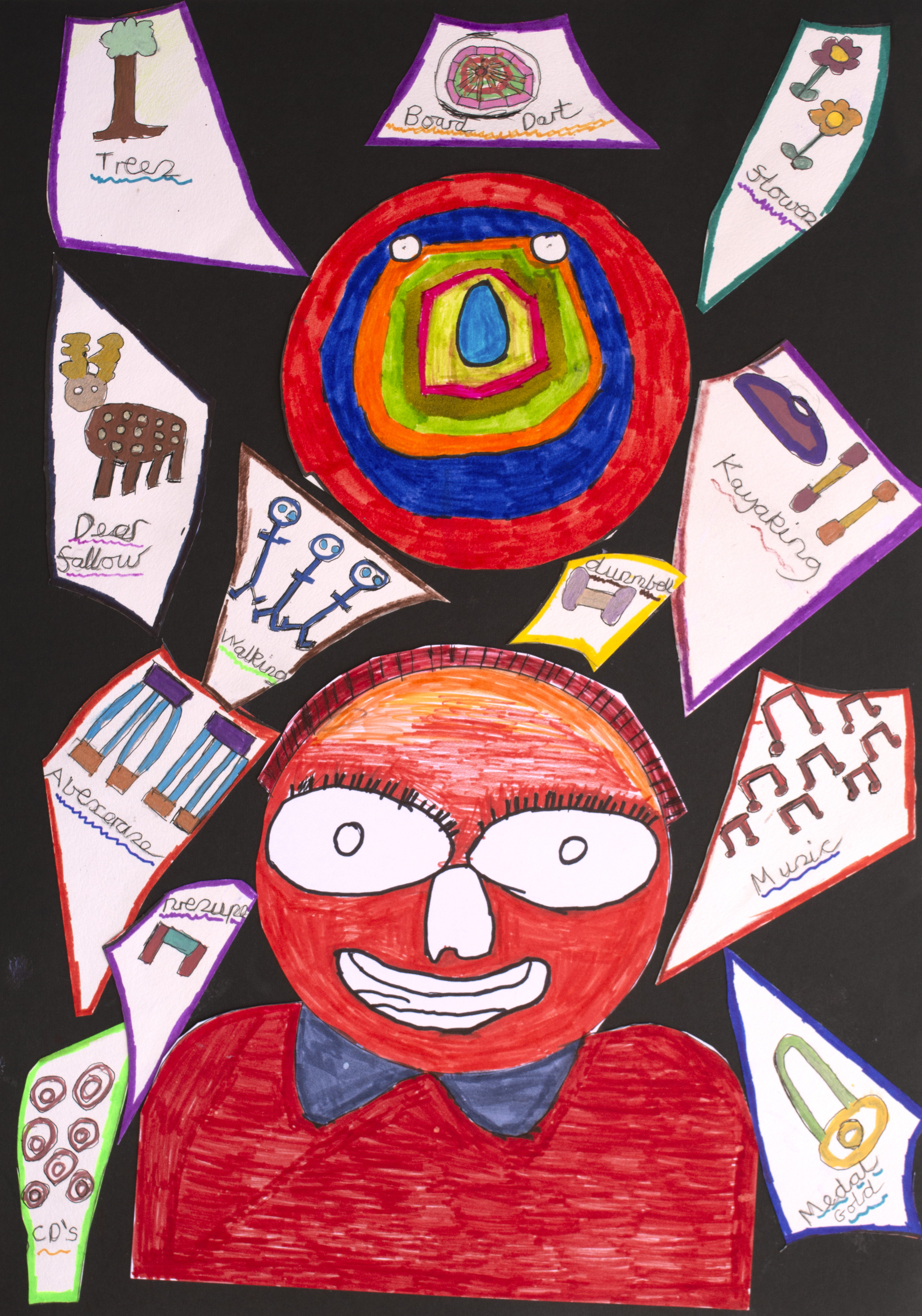 A child's collage on black paper featuring a large, bright orange-red cartoon face at the bottom. Surrounding the head are various hand-drawn cut-outs labelled with words like Tree, Dart Board, Walking, Kayaking, Music, and Gold Medal.