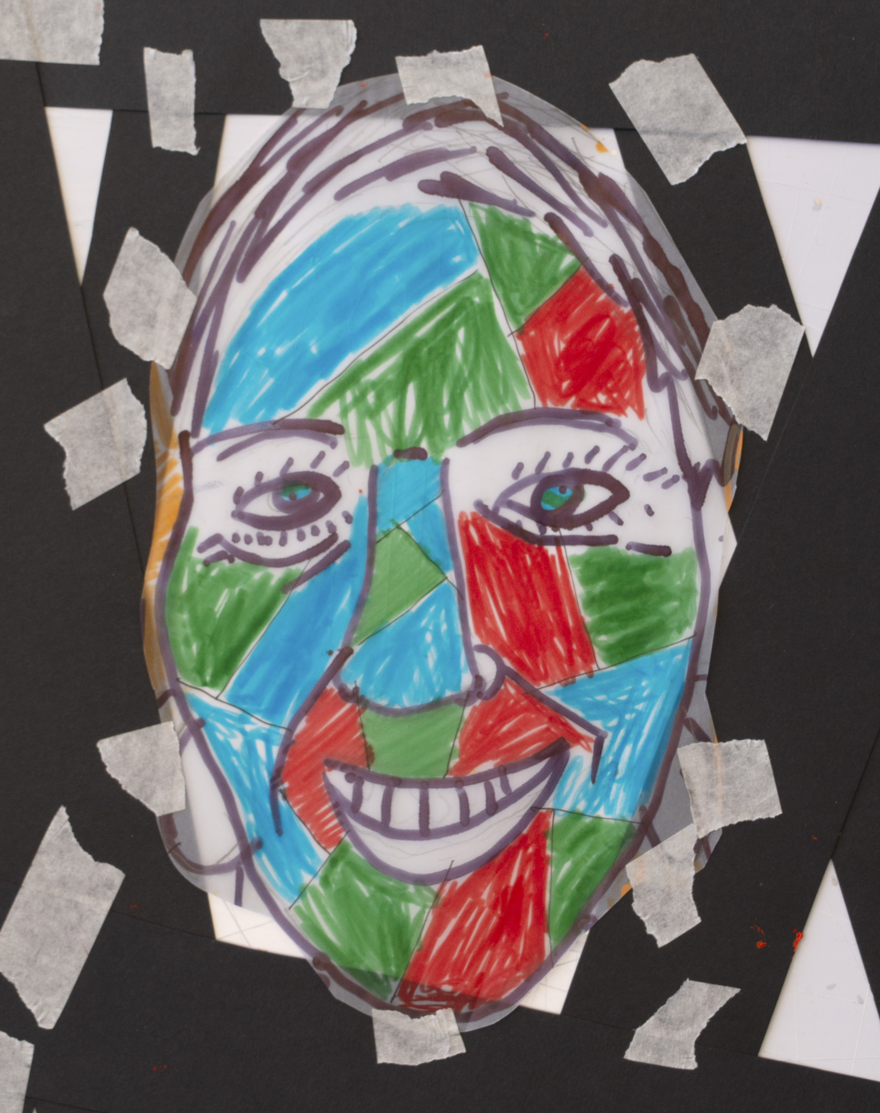 A colourful abstract face drawing with red, blue, and green sections, outlined in black, is taped onto a black background using several pieces of masking tape.