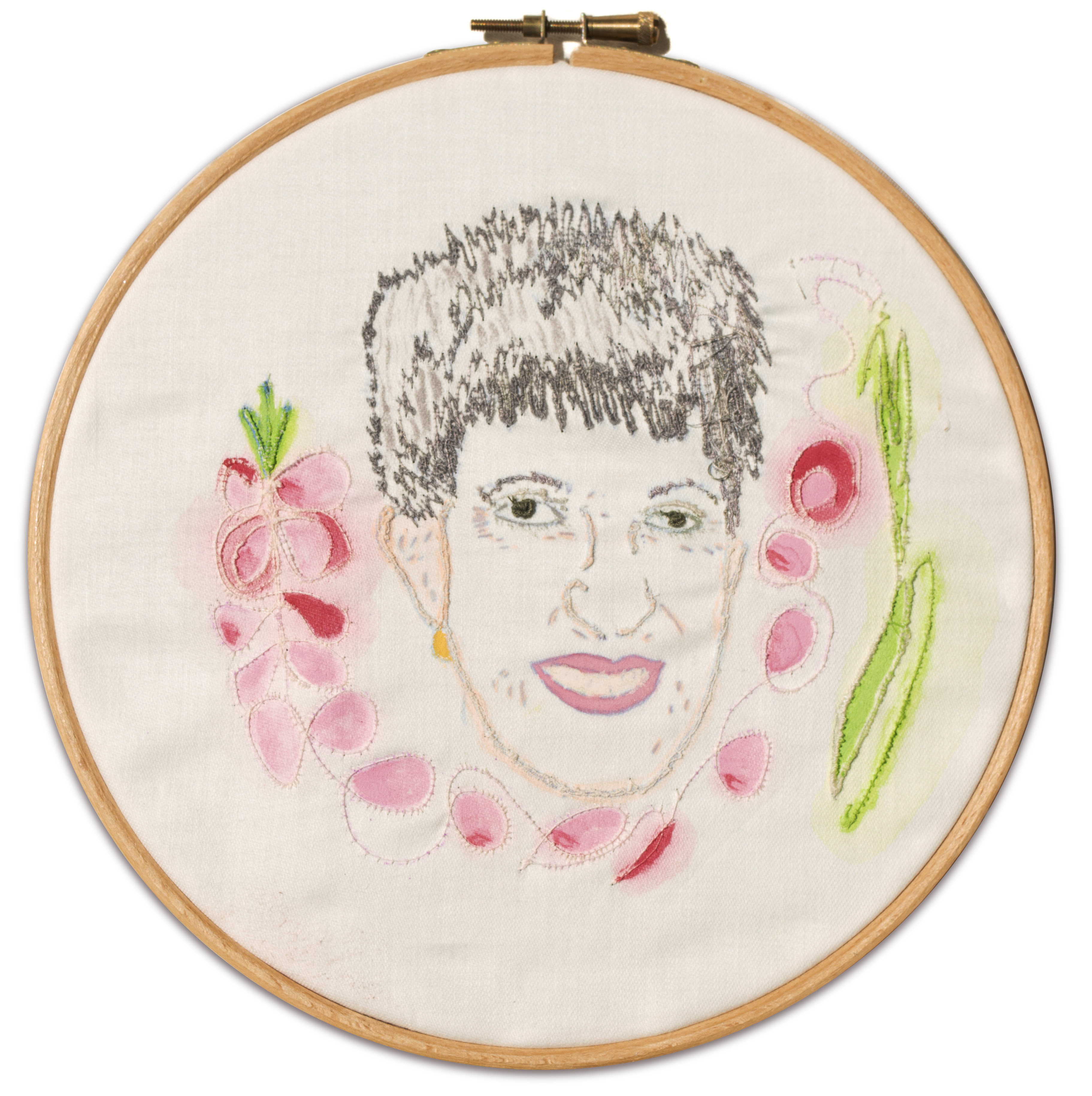 Embroidery hoop with a stitched portrait of a person, featuring short dark hair, smiling lips, and surrounded by pink and green abstract shapes on white fabric.